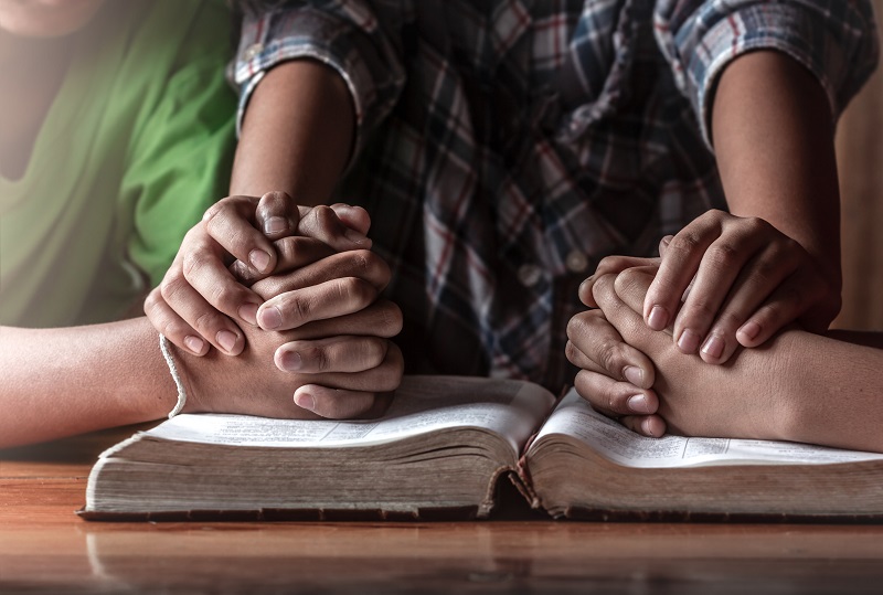christian young group praying on wooden table with open bible, prayer meeting concept